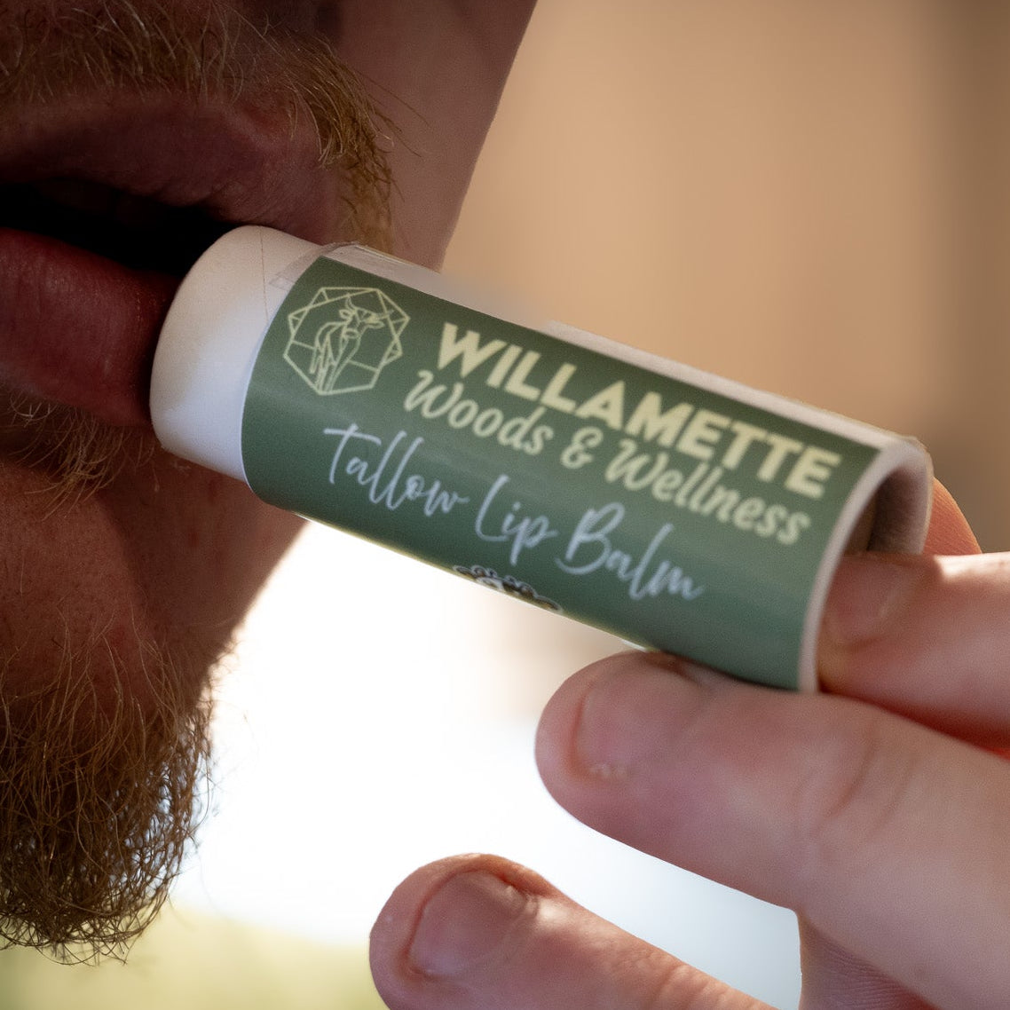 Person holding a Willamette Woods & Wellness lip balm stick against a blurred background