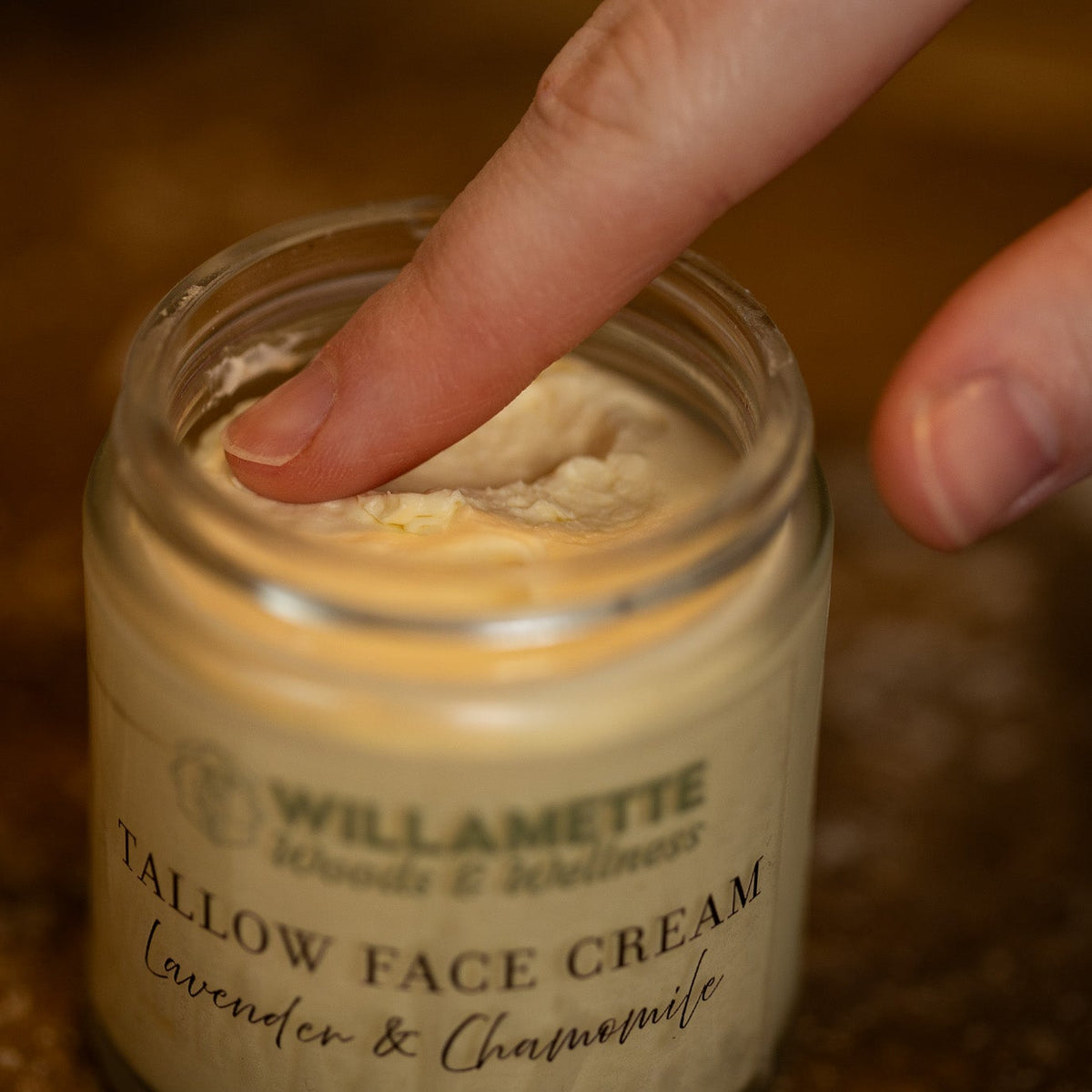 single finger dipping into a jar of tallow face cream