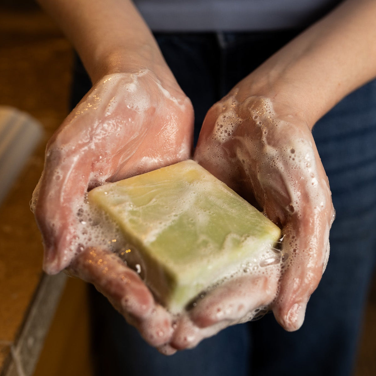 Hands holding a bar of soap with soap suds, on a blurred background