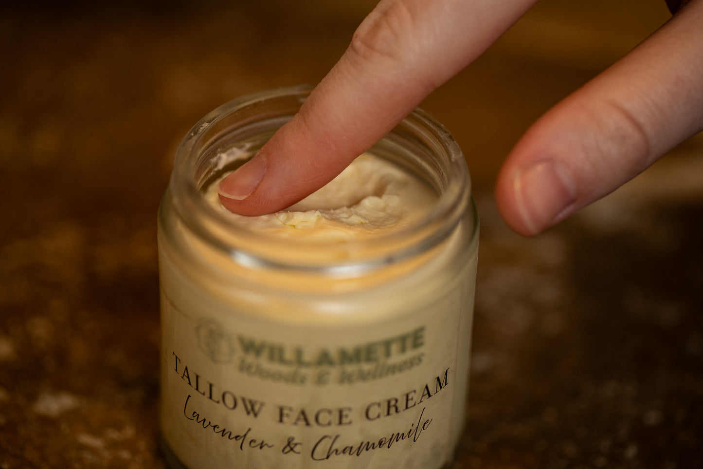 single finger dipping into a jar of tallow face cream