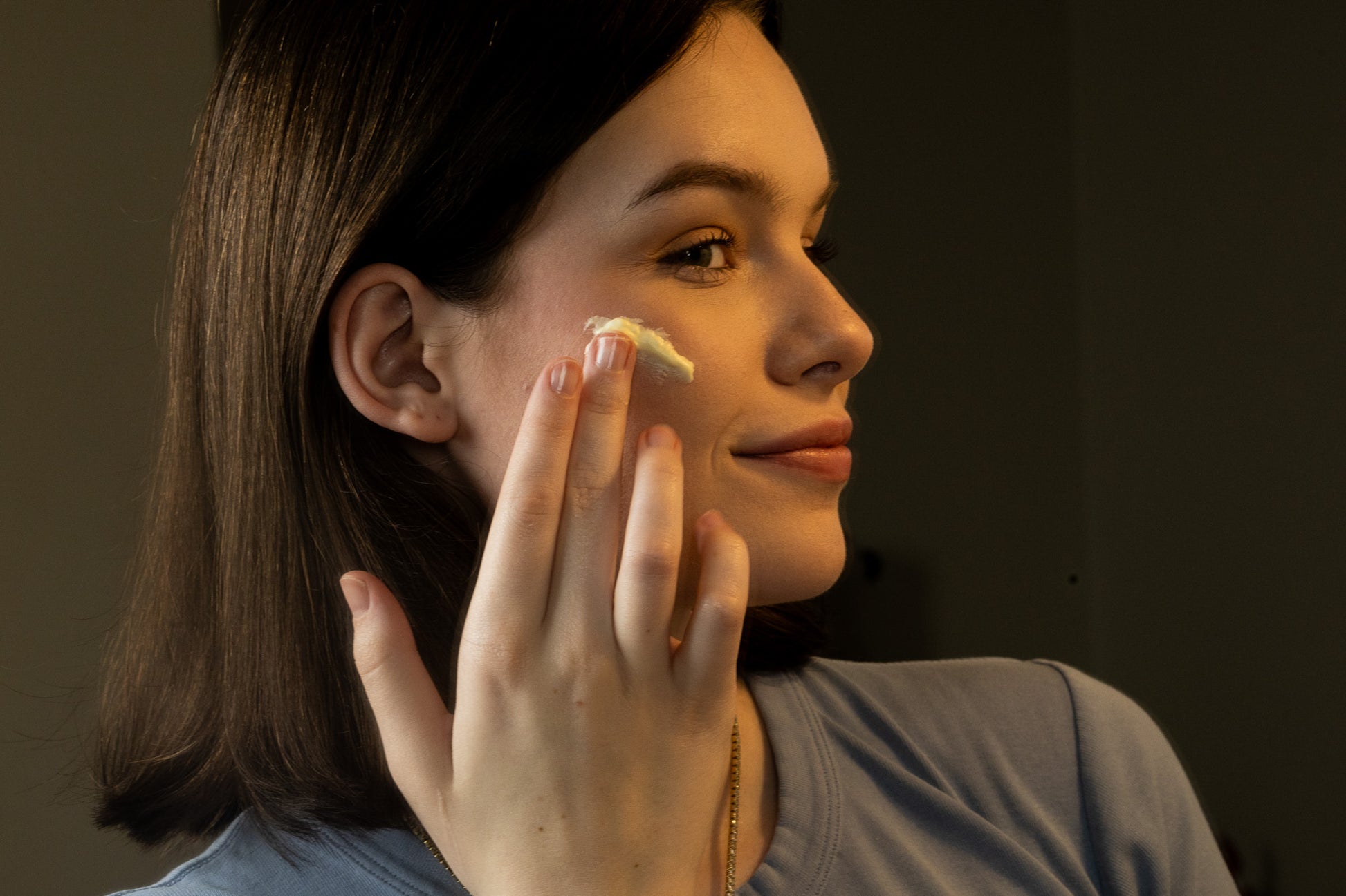 young woman putting tallow face cream on her face