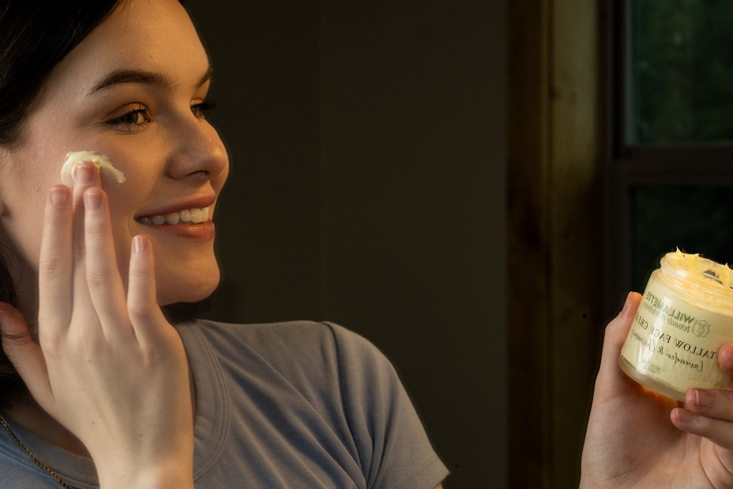 Young woman putting tallow on her face with jar in sight